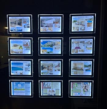 Suspended hanging LED window display installed in real estate office window showcasing property listings